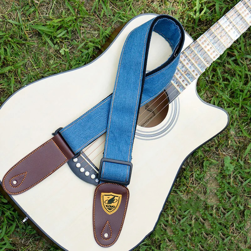 A dark blue denim strap for an acoustic guitar.